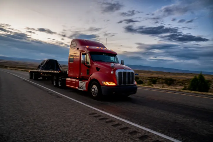 Red Peterbilt tractor pulling a loaded flatbed trailer on an Oklahoma highway — Bledsoe Truck & Trailer Repair services flatbeds, dry vans, reefers, and lowboys in the OKC metro.